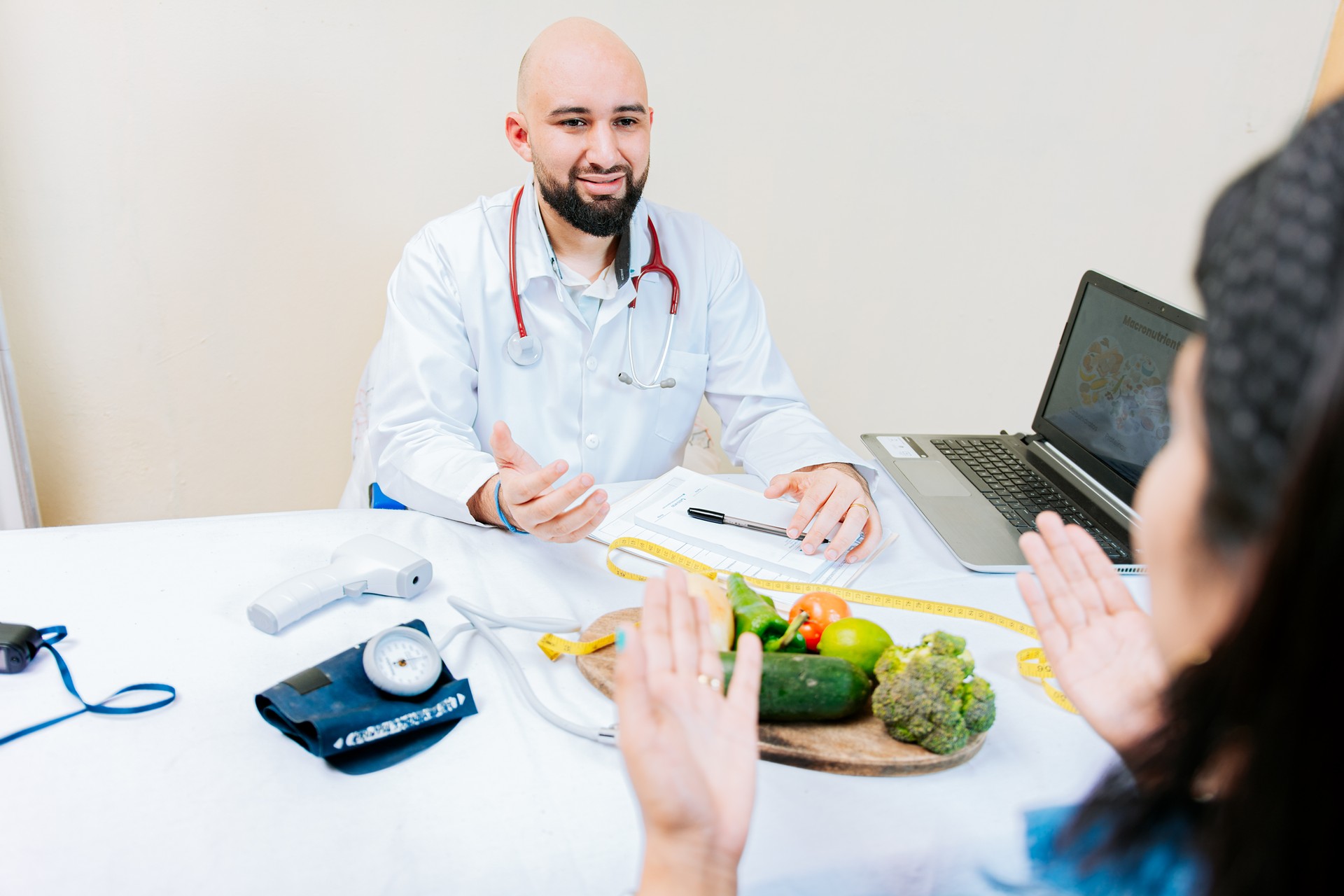 Nutritionist man talking to woman patient in office. Back view of a female patient talking to the nutritionist. Smiling nutritionist explaining to a female patient